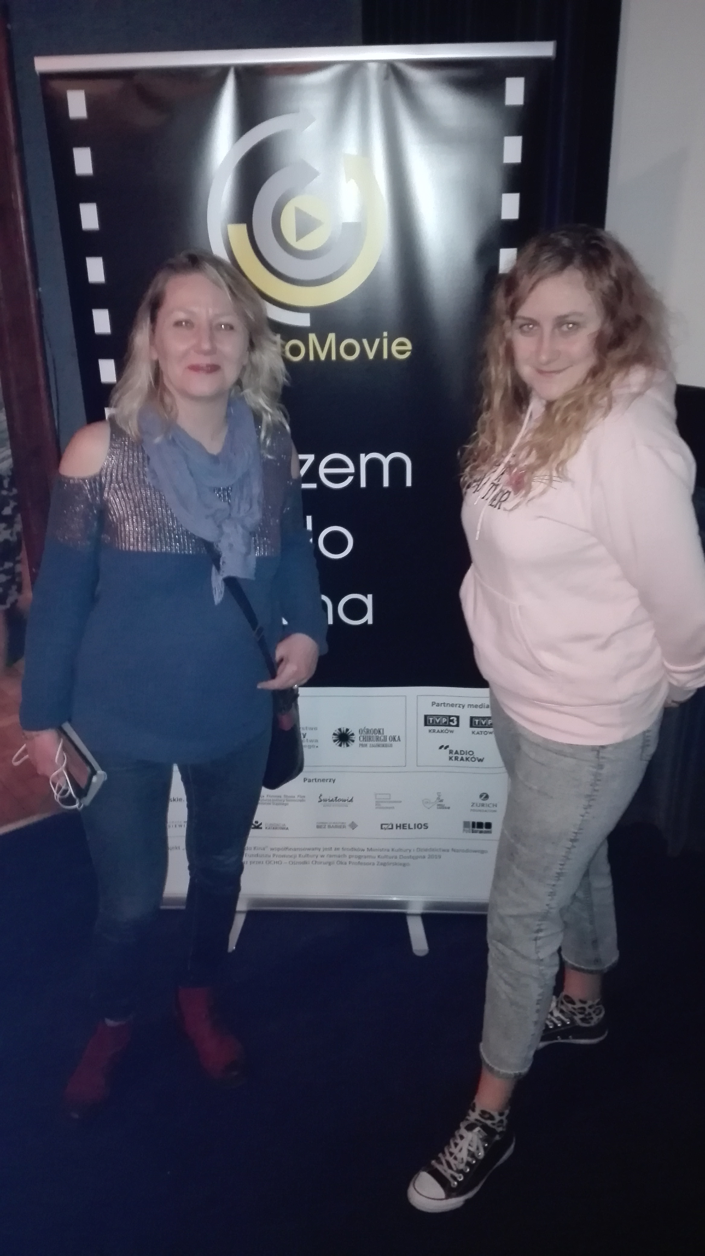 Alicja i Regina stoją na tle plakatu AudioMovie w kinowej sali.